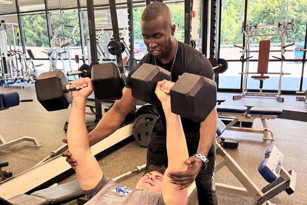 Man lifting dumb bells in workout with personal trainer at Steel Fitness Main Line in West Conshohocken